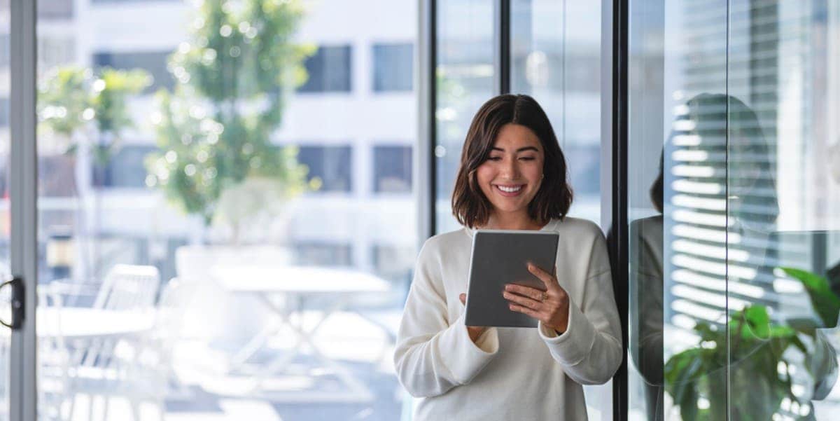 woman standing by window, looking at tablet