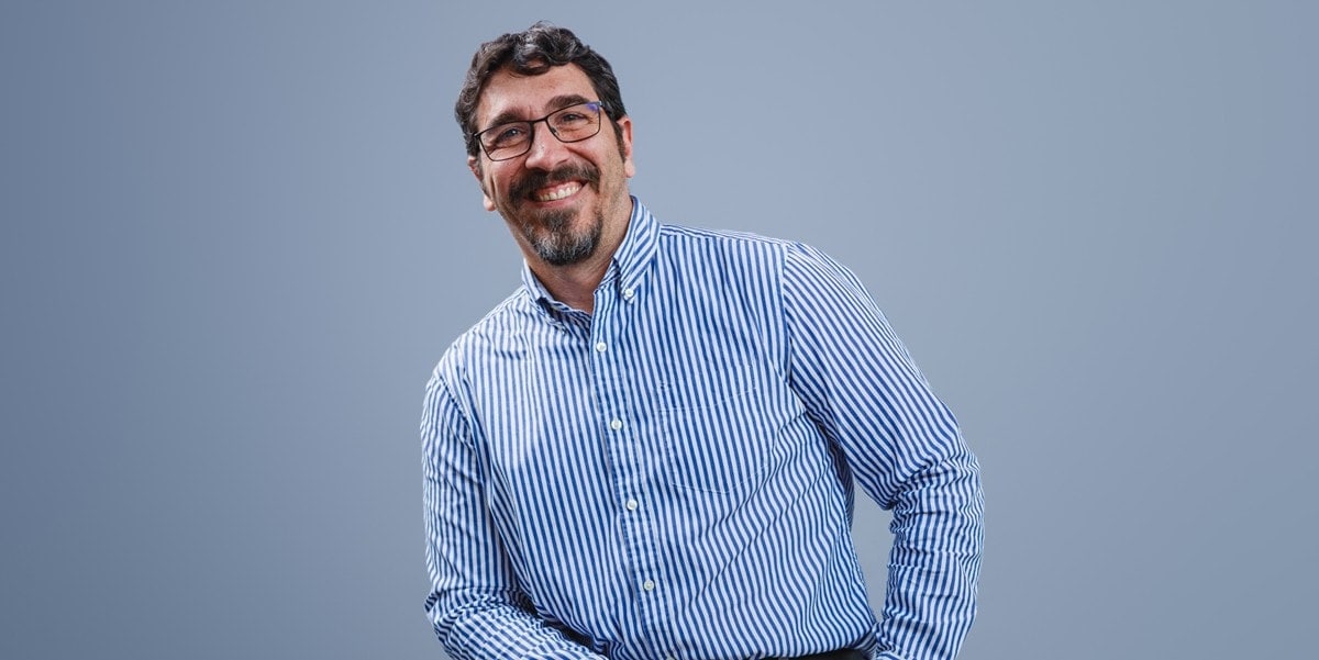 professional man smiling, sitting in front of blue wall